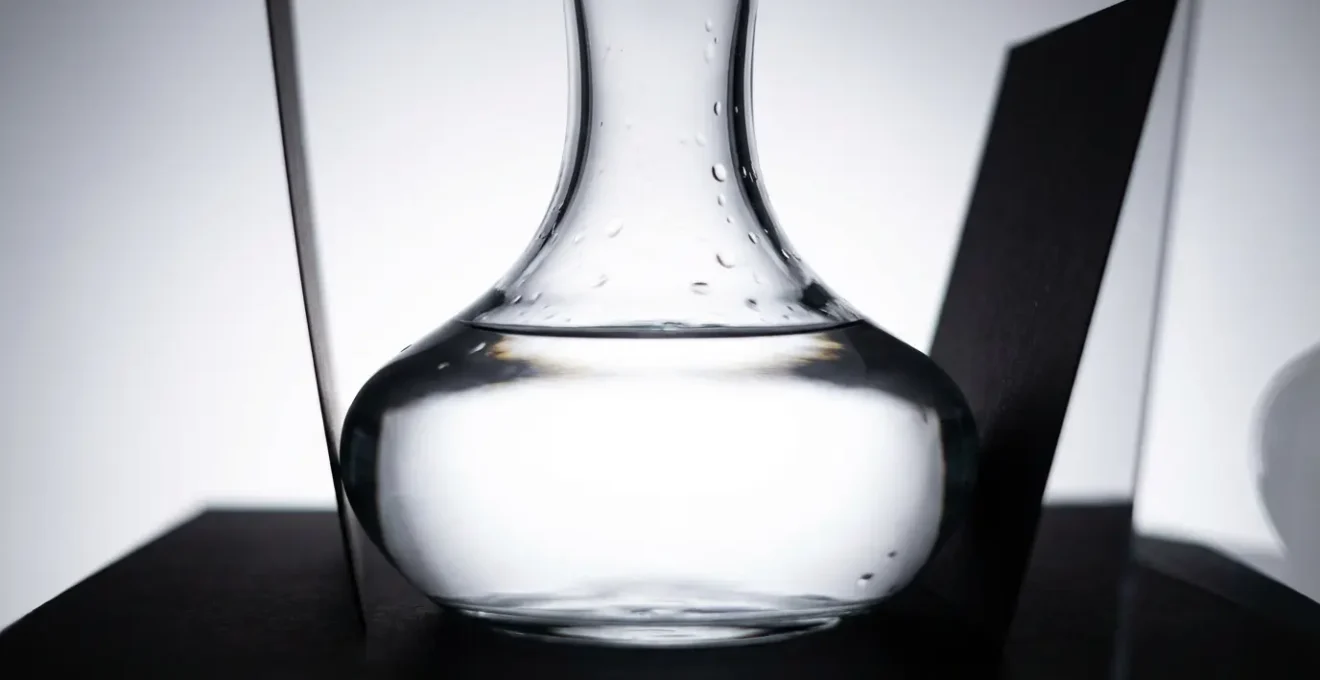 Carafe en verre transparent éclairée par technique de soustraction par le noir, avec des lignes sombres nettes définissant sa silhouette sur fond clair